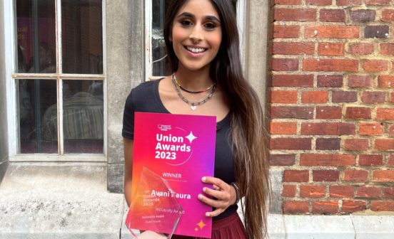 Avi standing in front of a brick building, holding the award and certificate